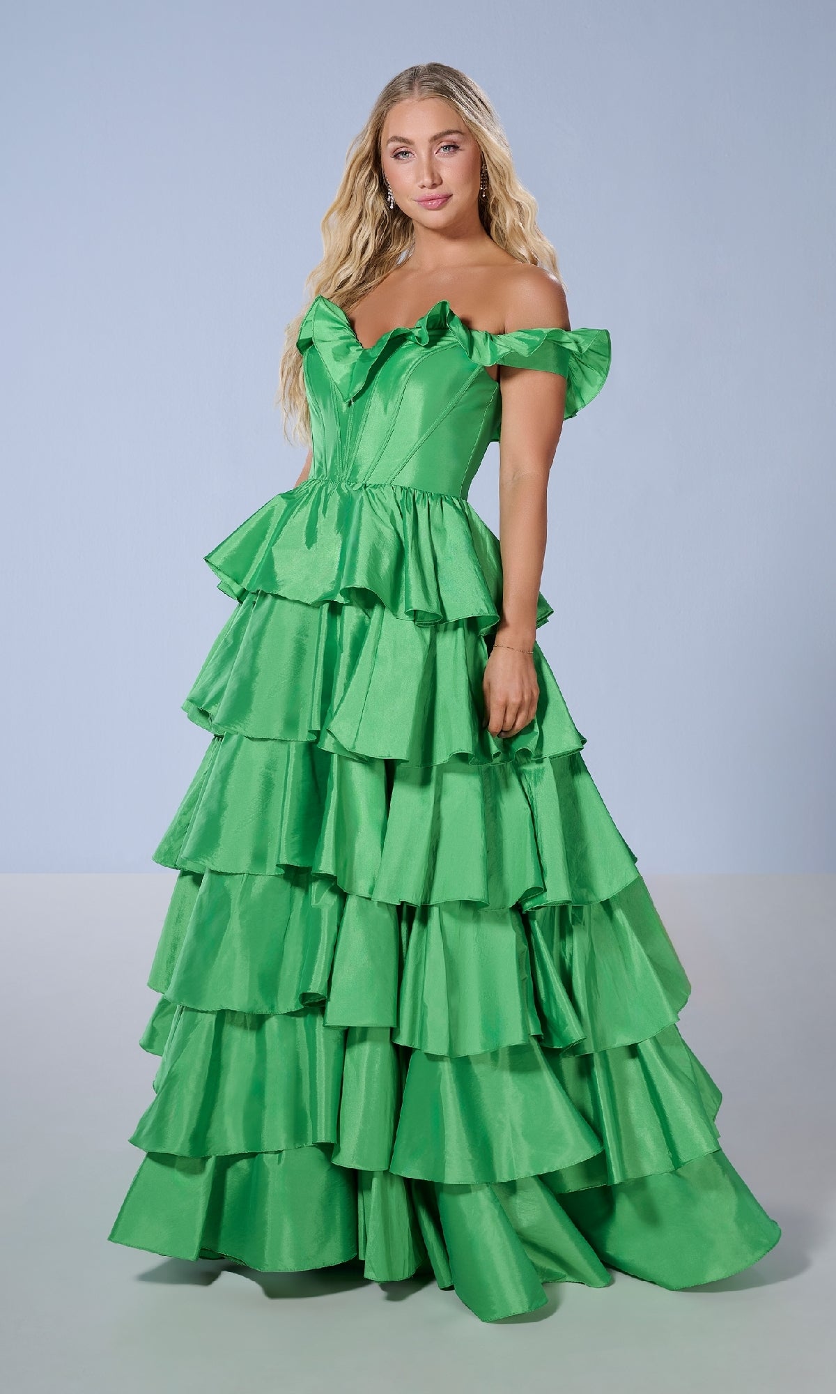 A woman stands in a studio against a plain light background, wearing the Long Prom Dress: Tiffany 16175—an off-the-shoulder, tiered bright green taffeta gown with ruffles.